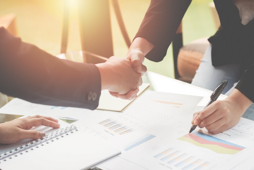 Two people shaking hands over a table full of documents.