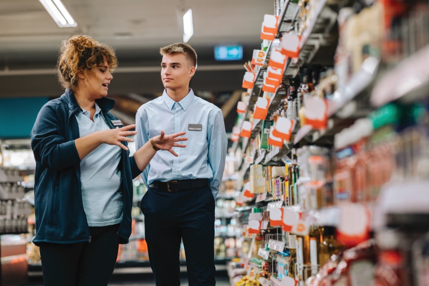 A supervisor trains a new employee at a retail grocery store.