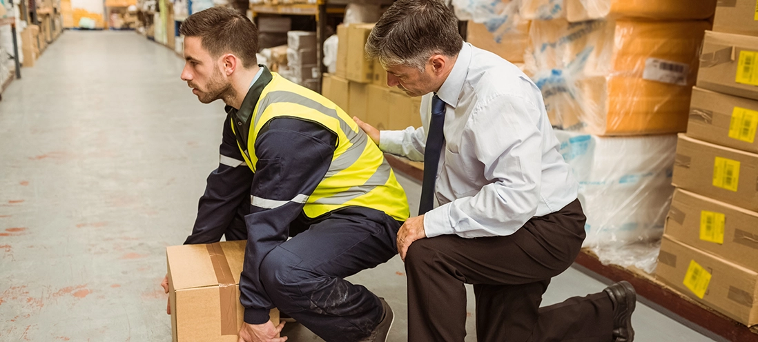 A supervisor instructs a warehouse employee on proper lifting techniques.
