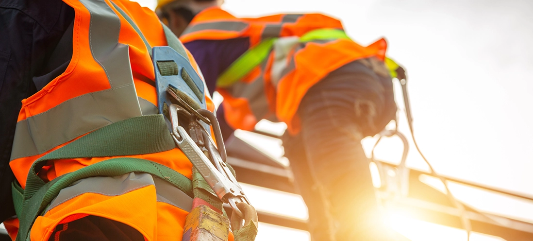 Two individuals in safety vests and harnesses work on an elevated structure.
