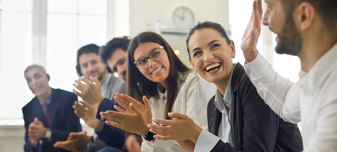 Group of smiling employees applaud for their coworker.