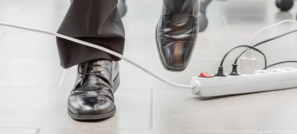Person tripping over a white electrical cord connected to a power strip on a tiled floor.