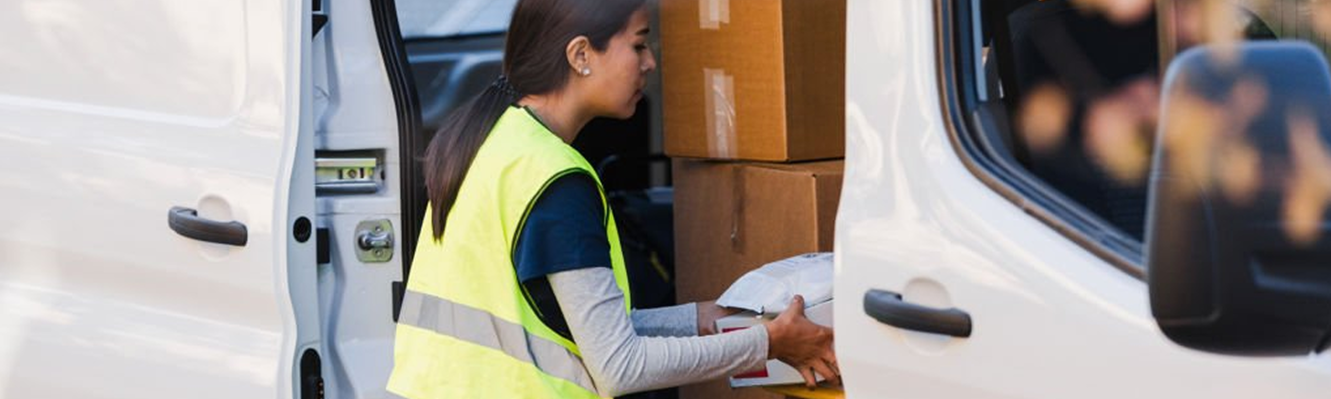 A delivery person in a high-visibility vest handling packages from the back of a van.