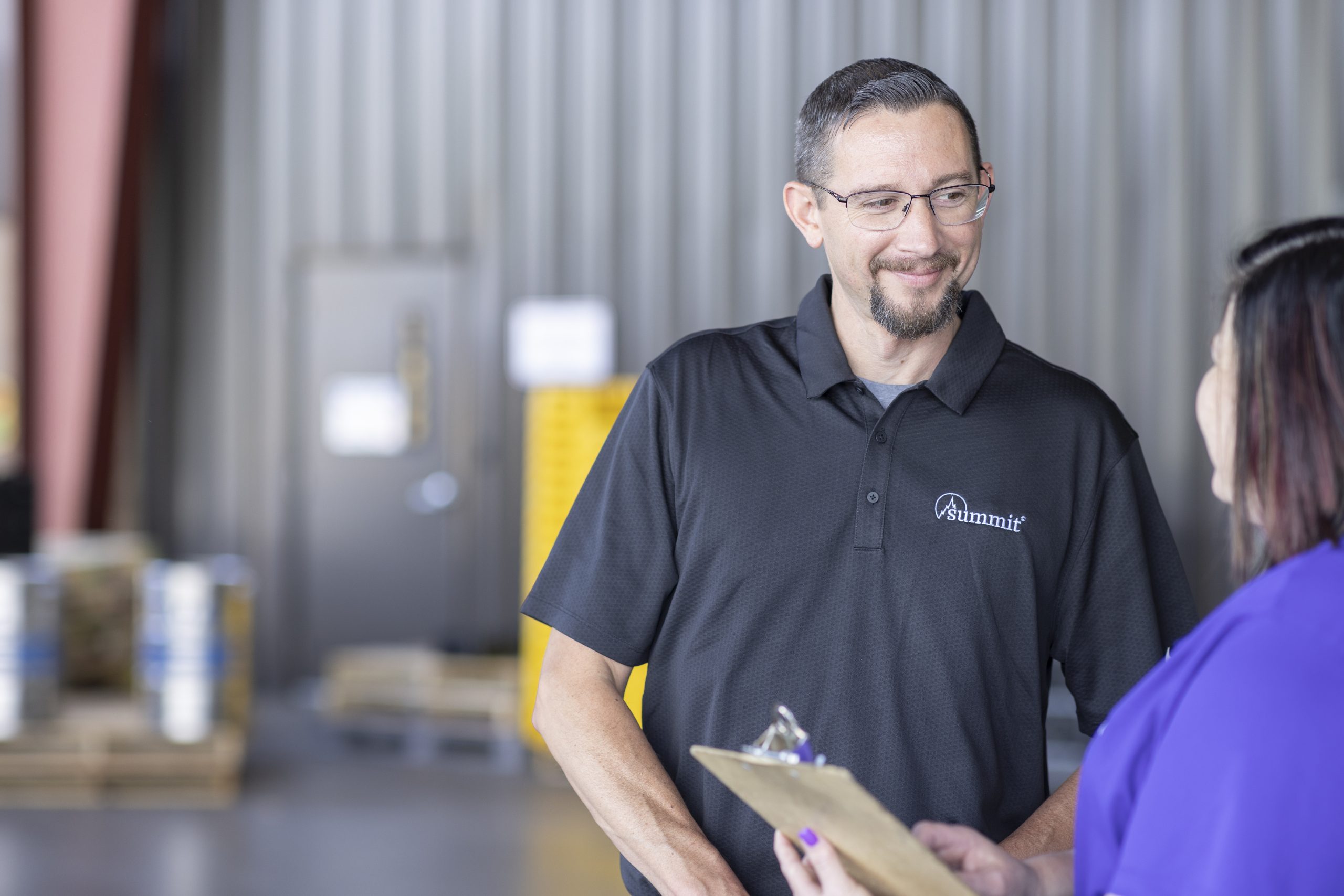 Summit consultant advises a policyholder holding a clipboard in a warehouse.