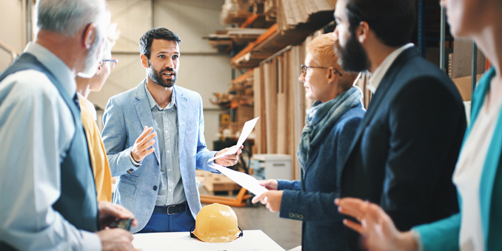 Consultant addresses a group of employees in a warehouse.